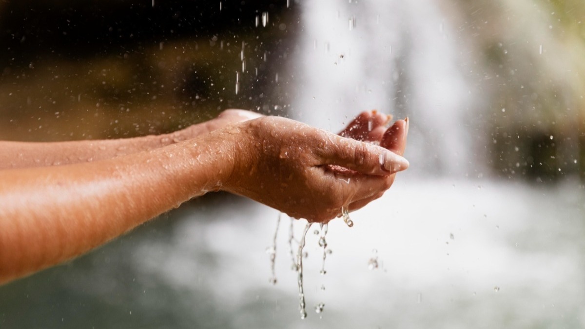 Close nas mãos de um jovem adulto perto da cachoeira, crise hídrica redação