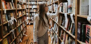 Importância da leitura - uma menina entre as estantes da biblioteca procurando um livro.