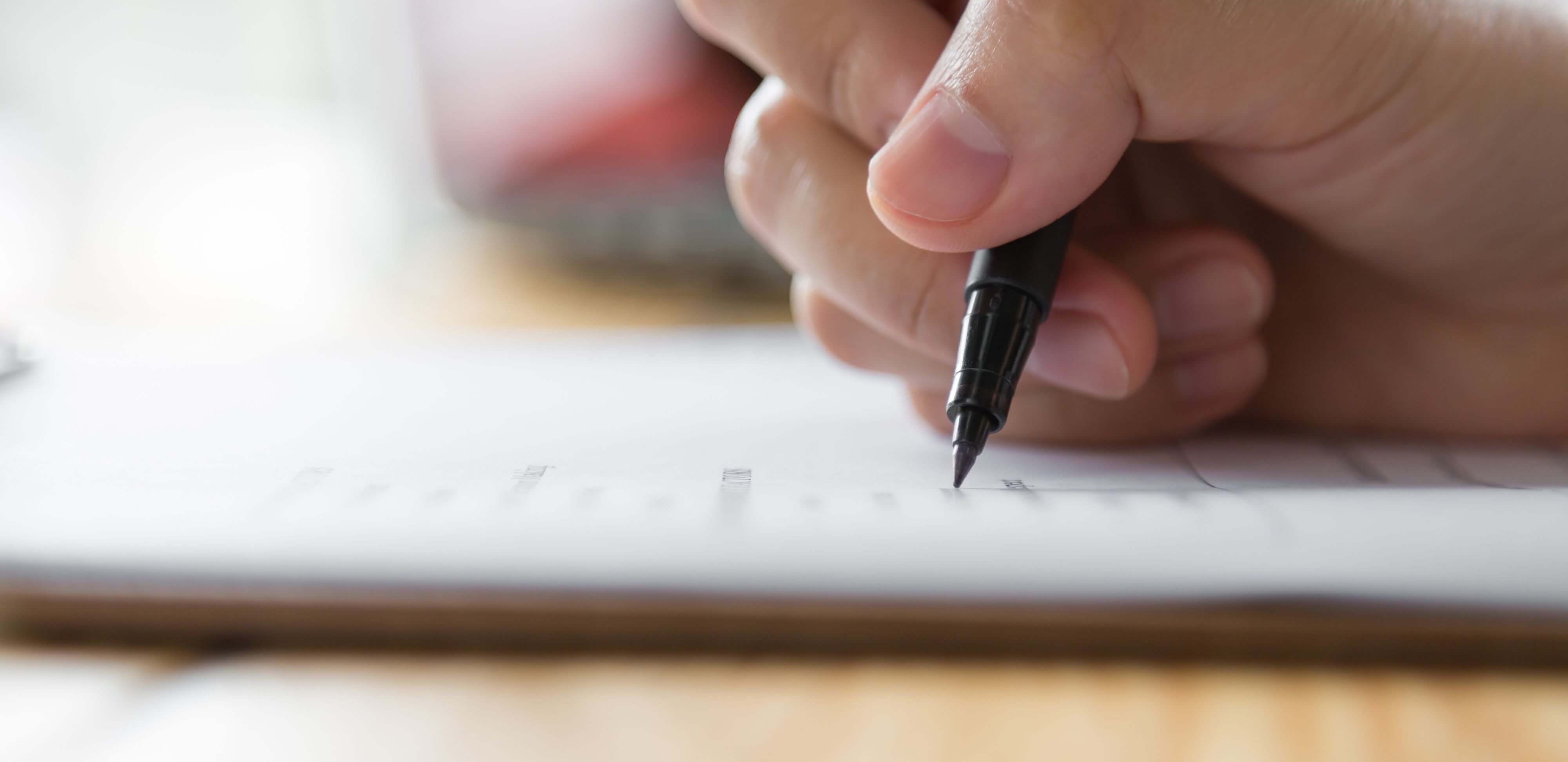 Regras de uma redação: fotografia de uma mão escrevendo uma redação com uma caneta.