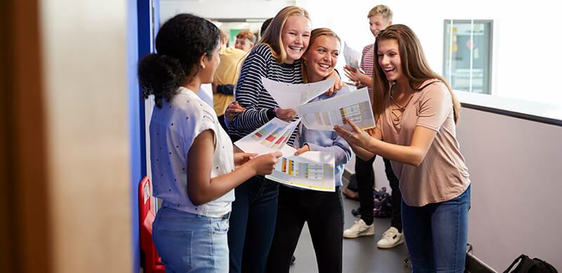Como fazer uma redação nota 1000: fotografia de 4 adolescentes comemorando em uma escola.