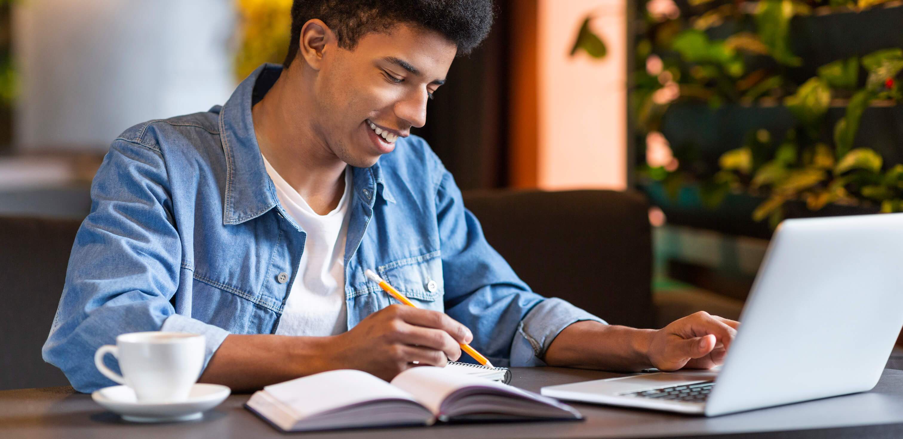 Curso de redação online: fotografia de um menino sorrindo enquanto escreve algo. À sua frente está um notebook.