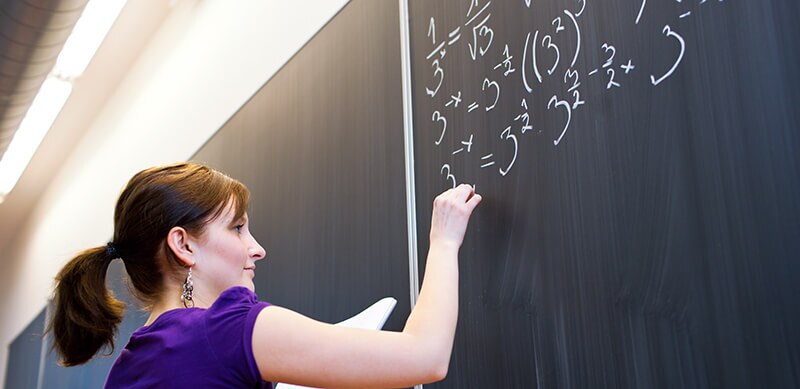 o que cai no segundo dia do Enem: fotografia de uma mulher resolvendo uma equação em um quadro negro.