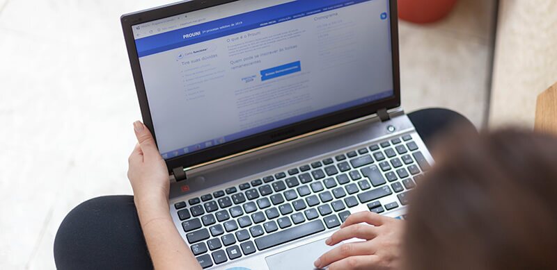 Fotografia de uma pessoa segurando o notebook que está com uma página do navegador aberta no site do Prouni.