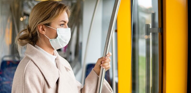 como o coronavírus pode cair no enem: moça de máscara segurando um apoio de transporte público