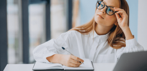 Citações por eixo temático: imagem de uma estudante com um notebook a sua frente e fazendo anotações no caderno.