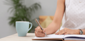 Combater o cansaço no momento de revisar textos: imagem de uma mulher escrevendo em um caderno.