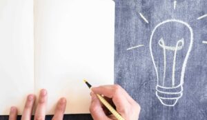 pessoa escrevendo no caderno e desenho de lâmpada ao lado, como ter inspiração para escrever