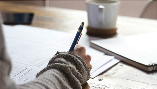 pessoa com um suéter cinza escrevendo em uma folha estudando palavras paroxítonas
