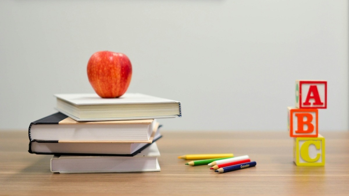 maçã em cima de 3 livros empilhados, com lápis de cor e blocos de letras na mesa, dia da escola